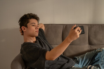 Fototapeta premium Boy holds phone horizontally recording short video for social media, blogging habit of whole young generation, gesture read without any caption. Wide shot. Concept of blogging habits of teenage boy