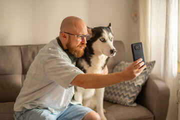 Man and his husky both look into phone screen during home selfie, blogging shot made in single second, mood every dog owner knows. Wide shot. Concept of blogging with dog for social media © iwavephoto