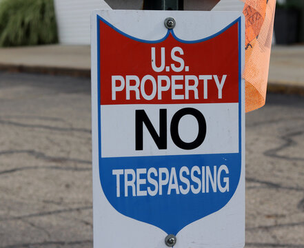 Shield shaped property warning sign reading US Property No Trespassing on post