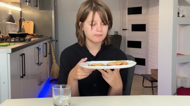 Young woman presenting plate of savory pastries at modern kitchen table, cozy home interior with neutral tones and gentle hand extension toward camera with soft warm light