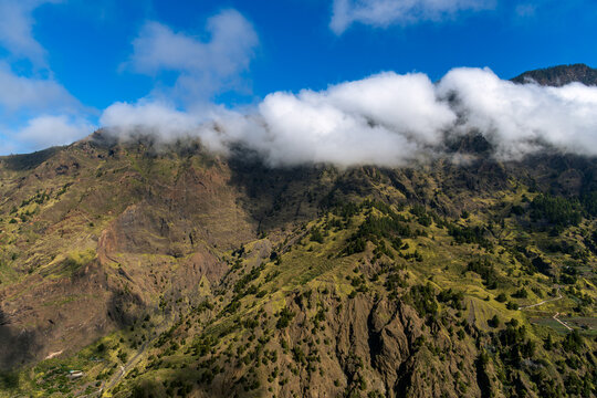 Thick white clouds rolling over steep volcanic mountain ridge in La Palma
