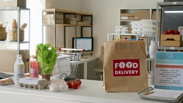 Paper bag with food delivery logo standing on supermarket counter beside fresh vegetables and eggs. Visual suits online grocery platform marketing and food delivery service advertising