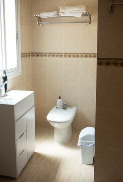 Bright tiled bathroom with bidet, vanity, towels, and sanitary fixtures in home interior