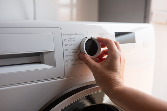 Hand Adjusting Washing Machine Dial On White Front Loading Laundry Appliance
