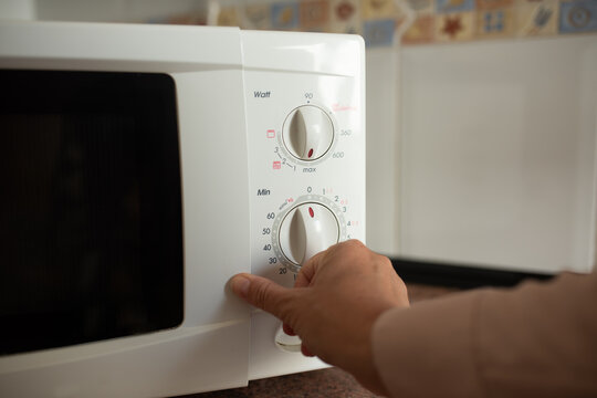 Hand Adjusting White Microwave Oven Controls in Domestic Kitchen Interior