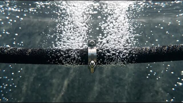 Underwater pipe releasing bubbles below a rippling surface with bright scattered reflections and dark water