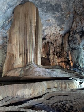 Impressive towering stalagmite and flowstone column formation inside an underground cave illuminated by artificial lighting.