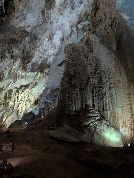 Close-up view of a massive towering stalagmite pillar and flowstone formation reaching toward the ceiling inside an illuminated limestone cave.