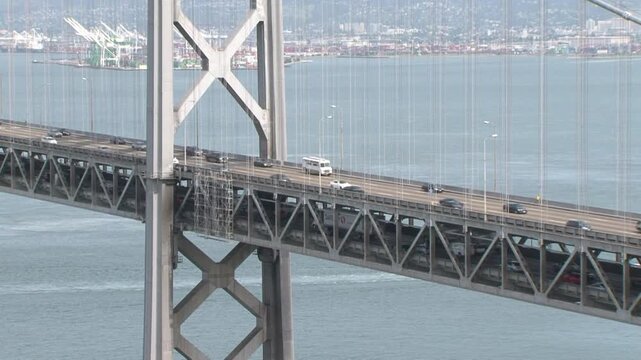This 2015 video framing focuses tightly on a steel suspension tower of the Bay Bridge. Traffic streams steadily across both the upper and lower multi-lane decks over the water. 