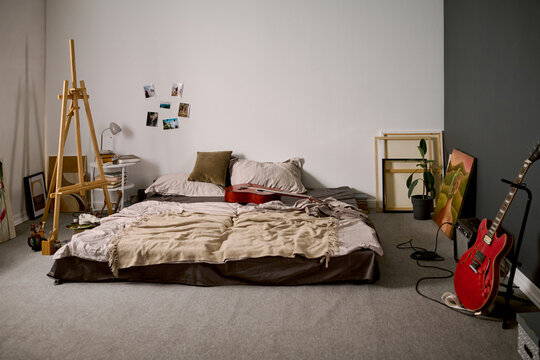 Creative bedroom studio featuring musical instruments, easel, and mattress on floor. Scene depicting artistic youth lifestyle, ideal for music or art advertising