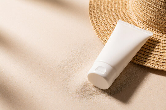 Unbranded sunscreen tube with straw hat on warm sandy background