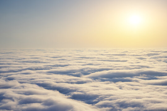 Bright sunrise sun shines over dense rolling clouds layer near dark mountain peak rocky silhouette. Golden dawn landscape