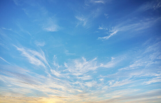 Thin white cirrus clouds scatter across vibrant blue sky with delicate cream gradient near horizon. Clear atmospheric texture