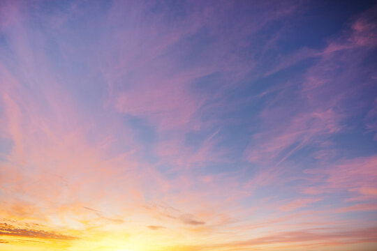 Soft lilac and pink feathery clouds drift across blue sky with bright lemon gradient near horizon during sunset. Dreamy atmospheric texture