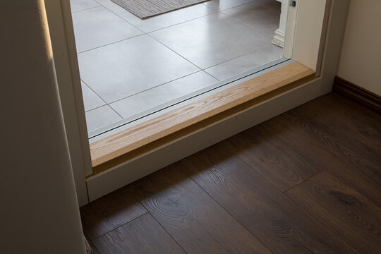 wooden threshold separates the tiled hallway from the living space's hardwood flooring. It creates a neat and professional visual boundary.