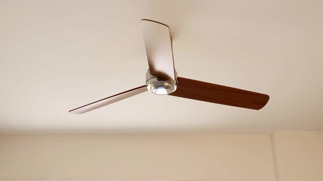 Slow motion static tracking shot of ceiling fan blades rotating and spinning on interior room ceiling