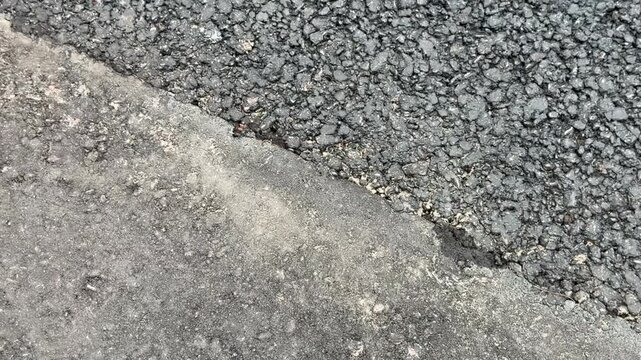 Close-up of a dark textured new asphalt next to an old grey concrete border or old pavement. road repair, construction material, street infrastructure.