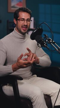 Portrait of happy young man talks in mic during podcast in radio studio vertical shot. Male host speaks about arts and culture in multimedia company office