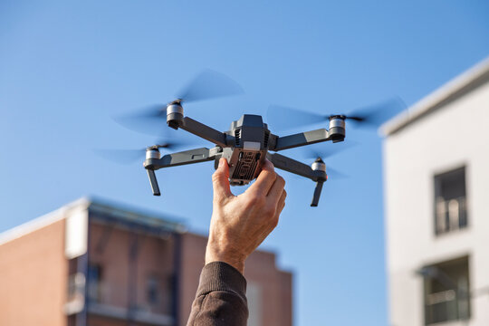 Person's hand releasing a drone into the blue sky with urban buildings in the background