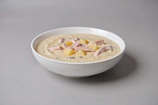 Cullen Skink in white bowl, filled with creamy yellow soup, garnished with sliced ham and diced mangoes. Concept of smoked haddock soup with potatoes cream, warmth and comfort.