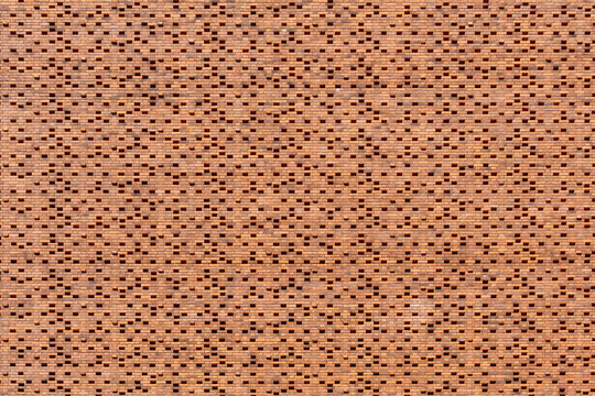 Terracotta brick wall with a modern perforated geometric pattern, creating a textured repeating facade with small openings for an architectural, industrial background
