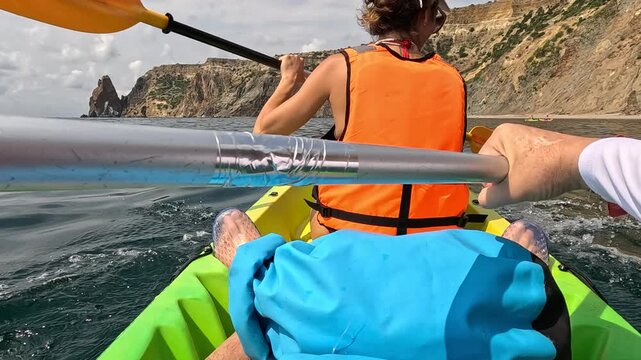 Dual rowing on vivid turquoise sea along stunning rocky cliffs under daylight. Action camera point-of-view perspective.