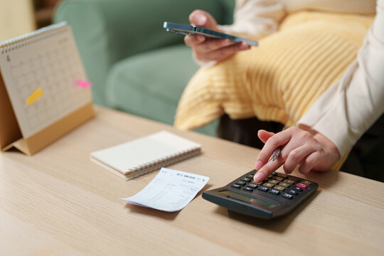 Woman using calculator and smartphone with receipt and calendar to review household expenses, personal debt and monthly payments, budgeting, repayment planning, financial pressure and money management