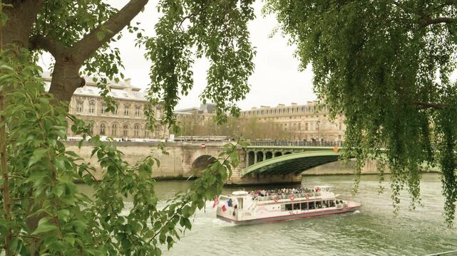 Seine River Cruise Boat Passing Under Historic Bridge Framed by Green Trees in Paris, France