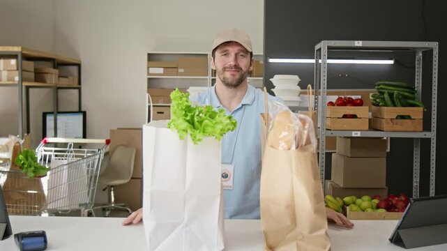 Portrait of young Caucasian clerk placing grocery paper bags on counter and smiling at camera. Ideal for food delivery service ads, online supermarket promos, or retail marketing