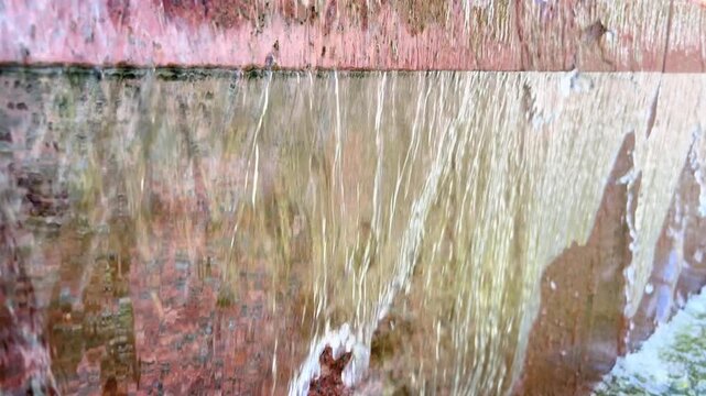 Close view of water streaming down textured red granite fountain wall