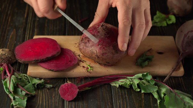 Hands of a person slicing a beetroot on a wooden cutting board, with vibrant red beet slices and fresh beet greens arranged around, creating a colorful and engaging kitchen scene