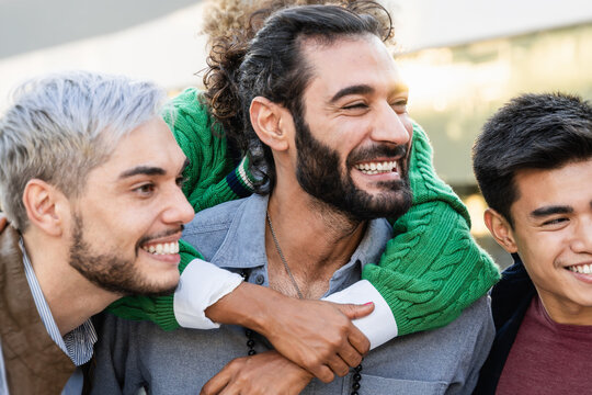 Happy multiracial friends having fun hugging outdoors outside university campus - Friendship, brotherhood, diversity and candid youth lifestyle - Soft focus on asian man eye