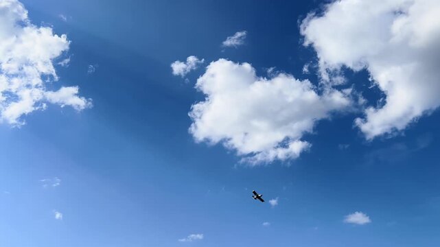 Distant small airplane crosses wide blue sky below large white summer clouds
