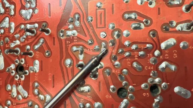 Soldering iron works across old red circuit board filled with metal joints