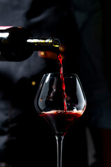 Fototapeta na wymiar Dry Sangiovese red wine pouring from dark bottle — luxury hospitality. Sommelier in apron with crystal glass serving premium beverage. Authentic restaurant experience, elegant celebration.