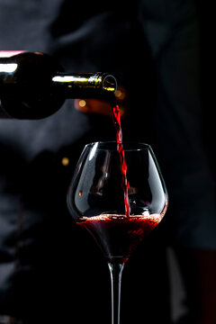Dry Sangiovese red wine pouring from dark bottle &mdash; luxury hospitality. Sommelier in apron with crystal glass serving premium beverage. Authentic restaurant experience, elegant celebration.