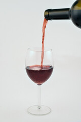 Obraz premium Red wine pouring from a dark bottle into an elegant clear glass on an isolated bright white background, symbolizing celebration, tasting, luxury, and fine dining.