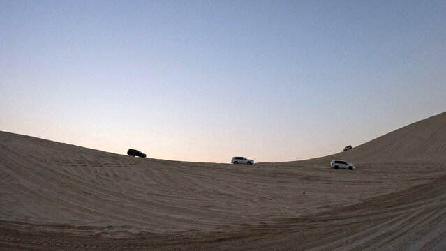 Four 4x4 SUVs Dune Bashing on a Tall Sand Dune Ridge at Dusk in the Qatar Desert