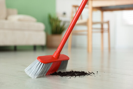 Sweeping soil with broom on floor indoors, closeup