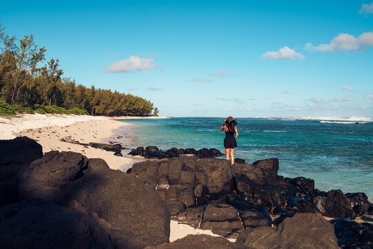 Woman Standing on Black Lava Rocks Watching a Dramatic Sunset on a Wild Beach, Mauritius