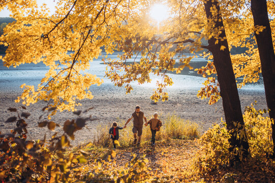 Father holding hands with his two kids during fall walk.