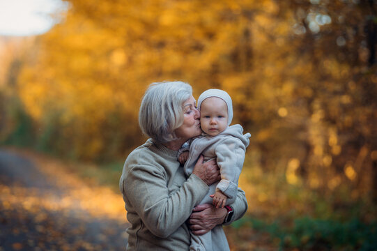 Grandmother kissing baby outdoors in autumn nature.