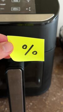 Hand holding percentage discount note over kitchen appliance