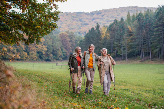 Old female friends enjoying countryside walk with walking poles.