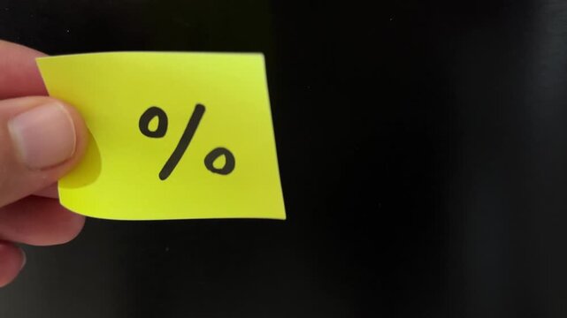 Hand holding percentage discount sticky note on black background