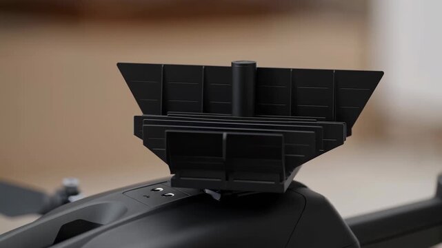 Black finned plastic attachment rotates slowly from angled view toward front-facing position on matte device housing, revealing layered dividers against warm blurred indoor background