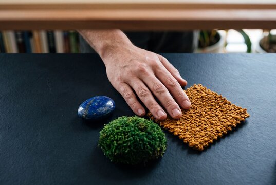 A male hand touching diverse natural textures including moss, fabric, and polished stone on a dark tabletop