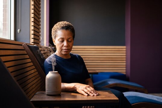 Mature African American woman relaxing in a modern spa lounge chair next to an essential oil aroma diffuser