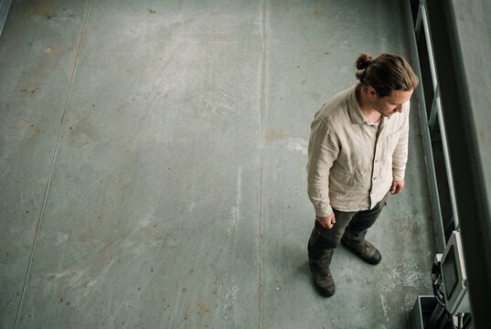High angle view of a young male technician standing on an industrial concrete floor looking at a digital control panel