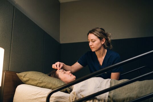 Caring female nurse tending to a sick female patient lying in a hospital bed with gentle medical care
